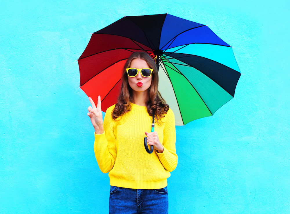 A woman in a bright yellow jumper holding a rainbow umbrella
