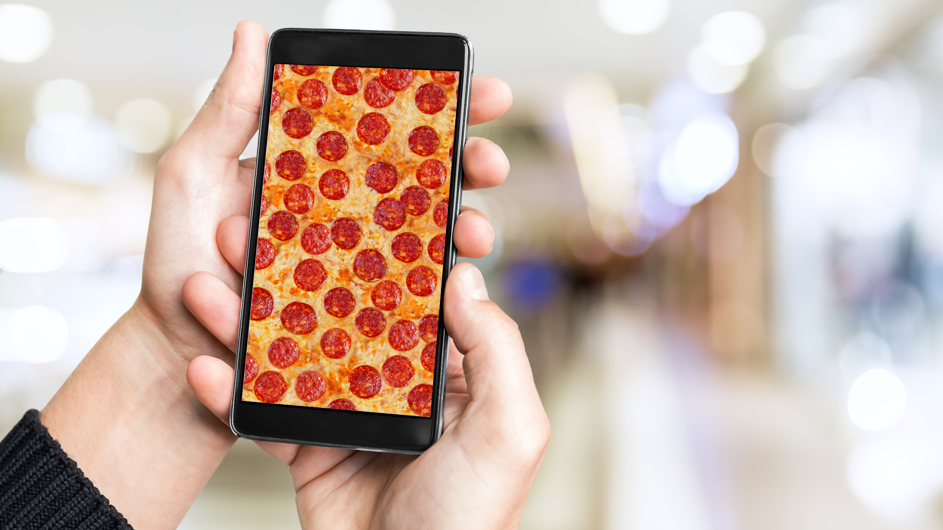 A person holding a mobile phone showing a slice of pizza