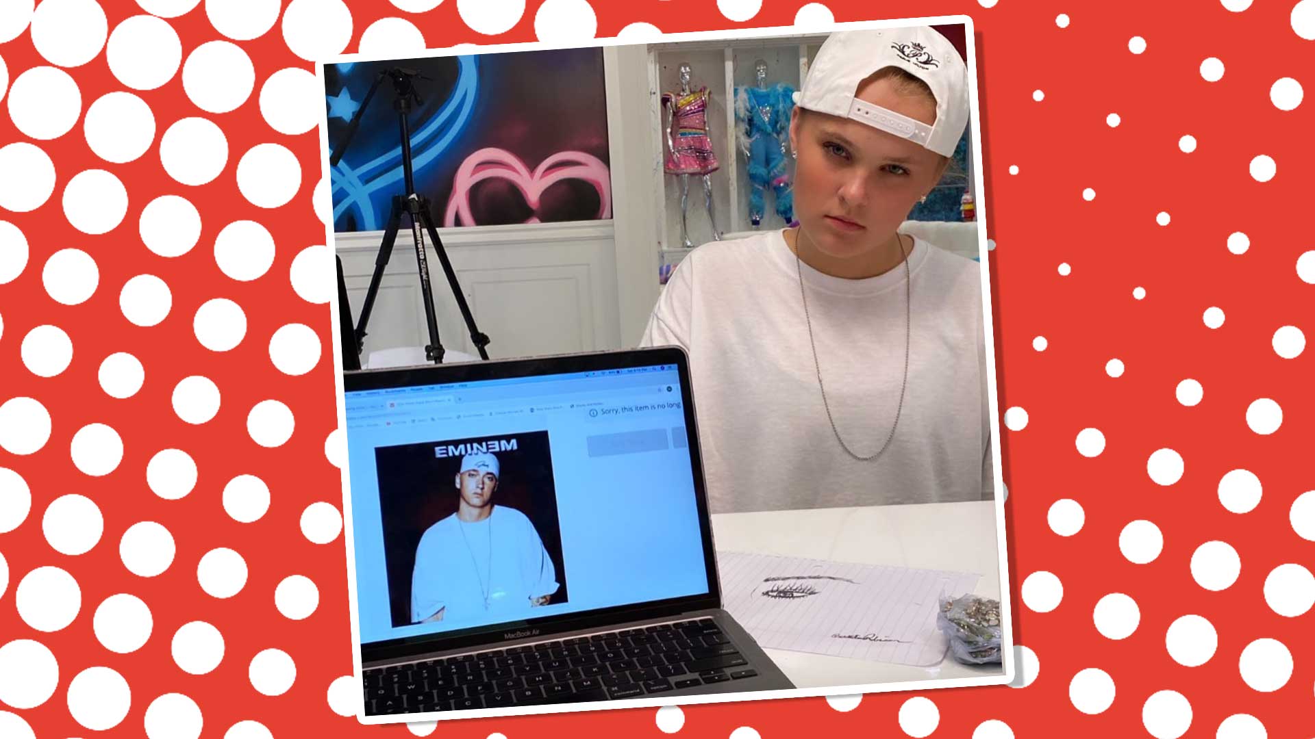 JoJo Siwa standing in front of a laptop which shows a picture of the rapper Eminem