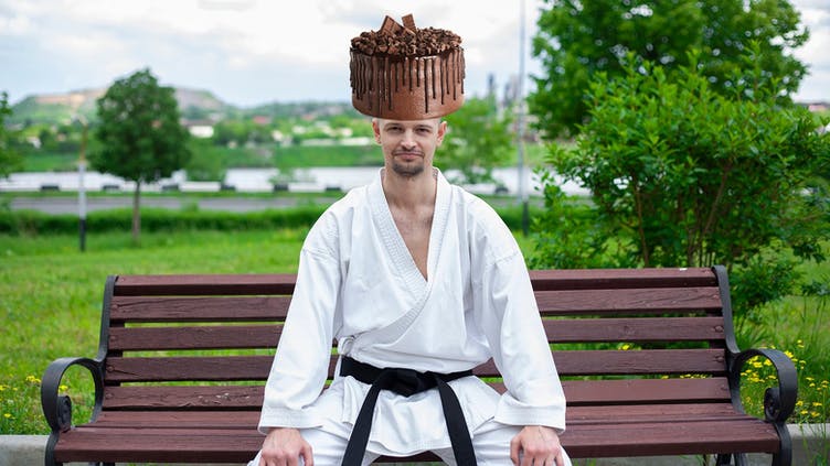 A man in a karate suit with a chocolate cake on their head