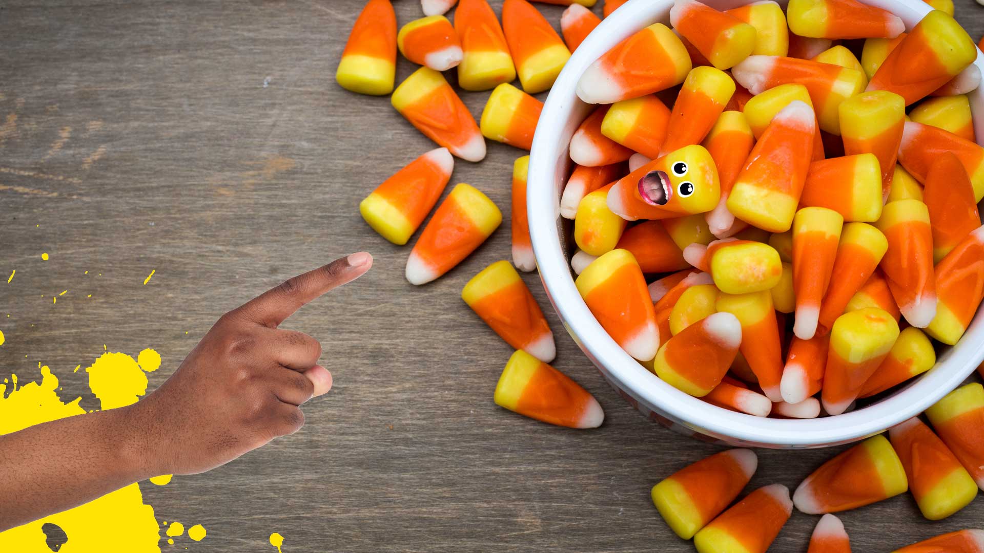A finger pointing at a bowl of candy corn