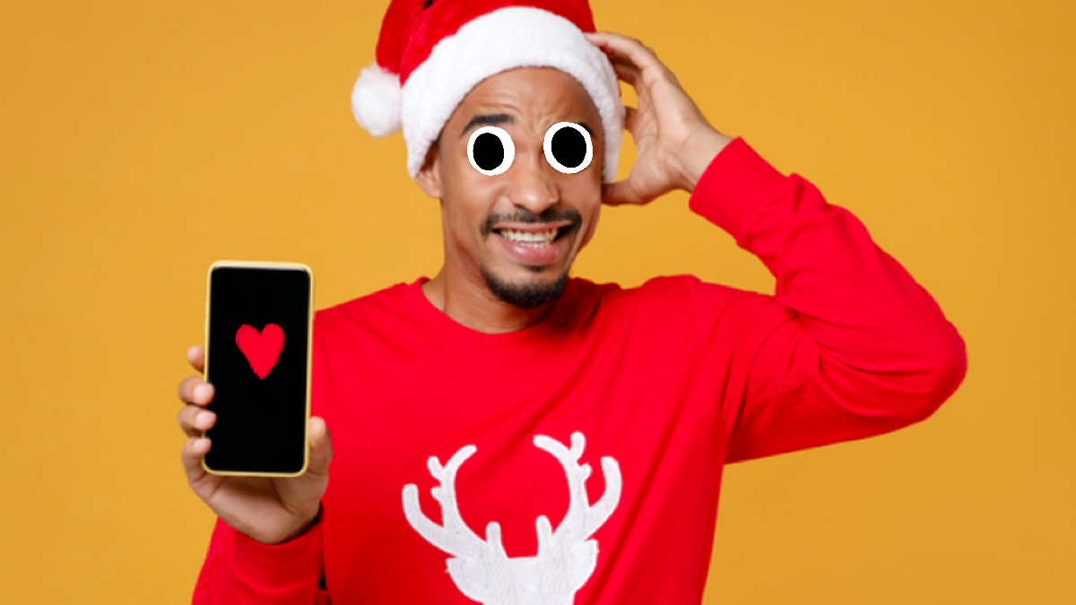 A man in a Christmas jumper holding a phone which shows a heart