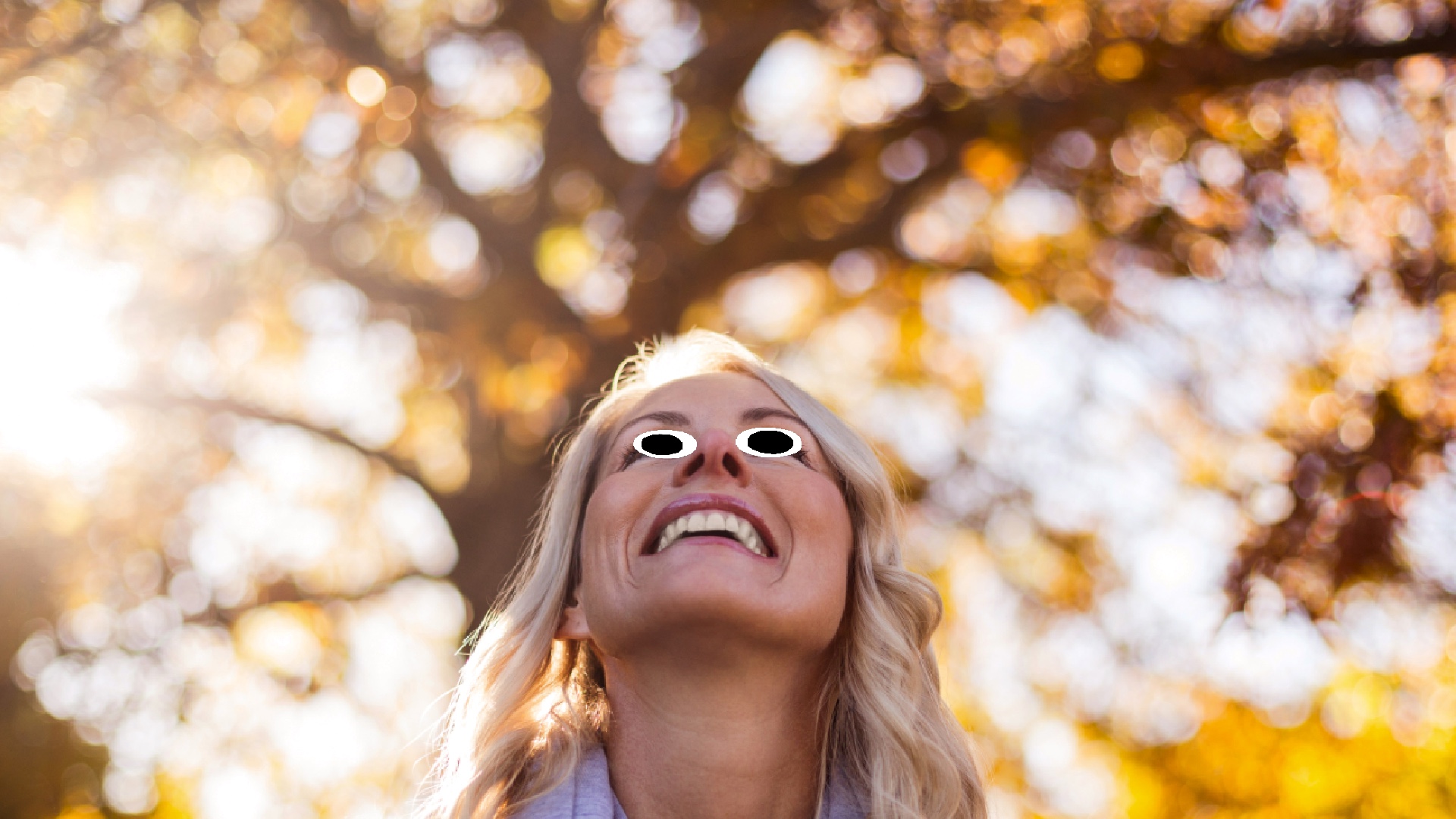 A woman stares up towards the sky, with autumnal trees in the background