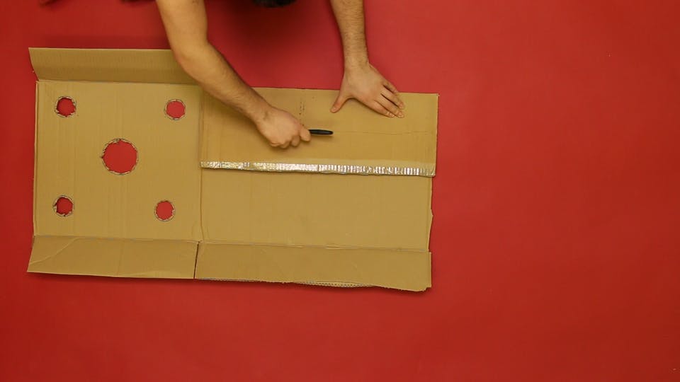 Cut holes in the top half of a sheet of cardboard, and fold and tape the flaps to create guard rails