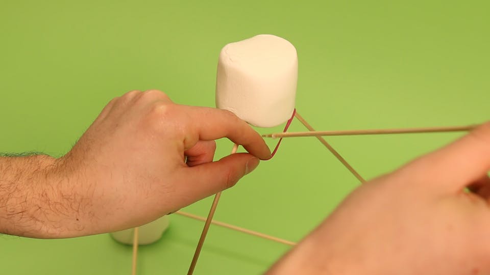 Stick the skewer (with the spoon) inside the rubber band, and poke it straight into the marshmallow at the base
