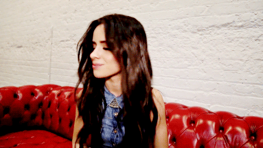 Camila Cabello shakes her hair on a red leather sofa 