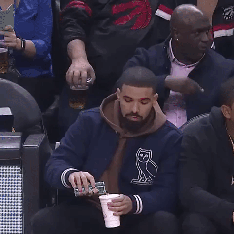 Drake looks awkward while pouring a drink at a basketball game