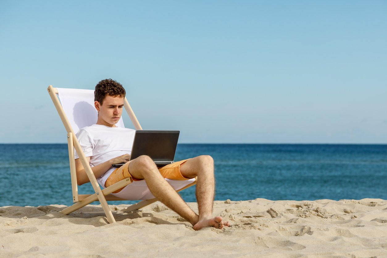 A man uses a laptop on the beach