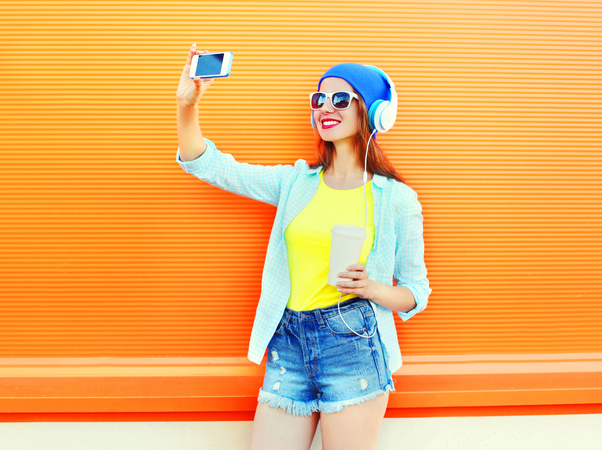 A woman takes a selfie against an orange background