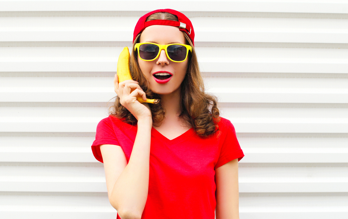 A woman in a red t-shirt using a banana as a phone