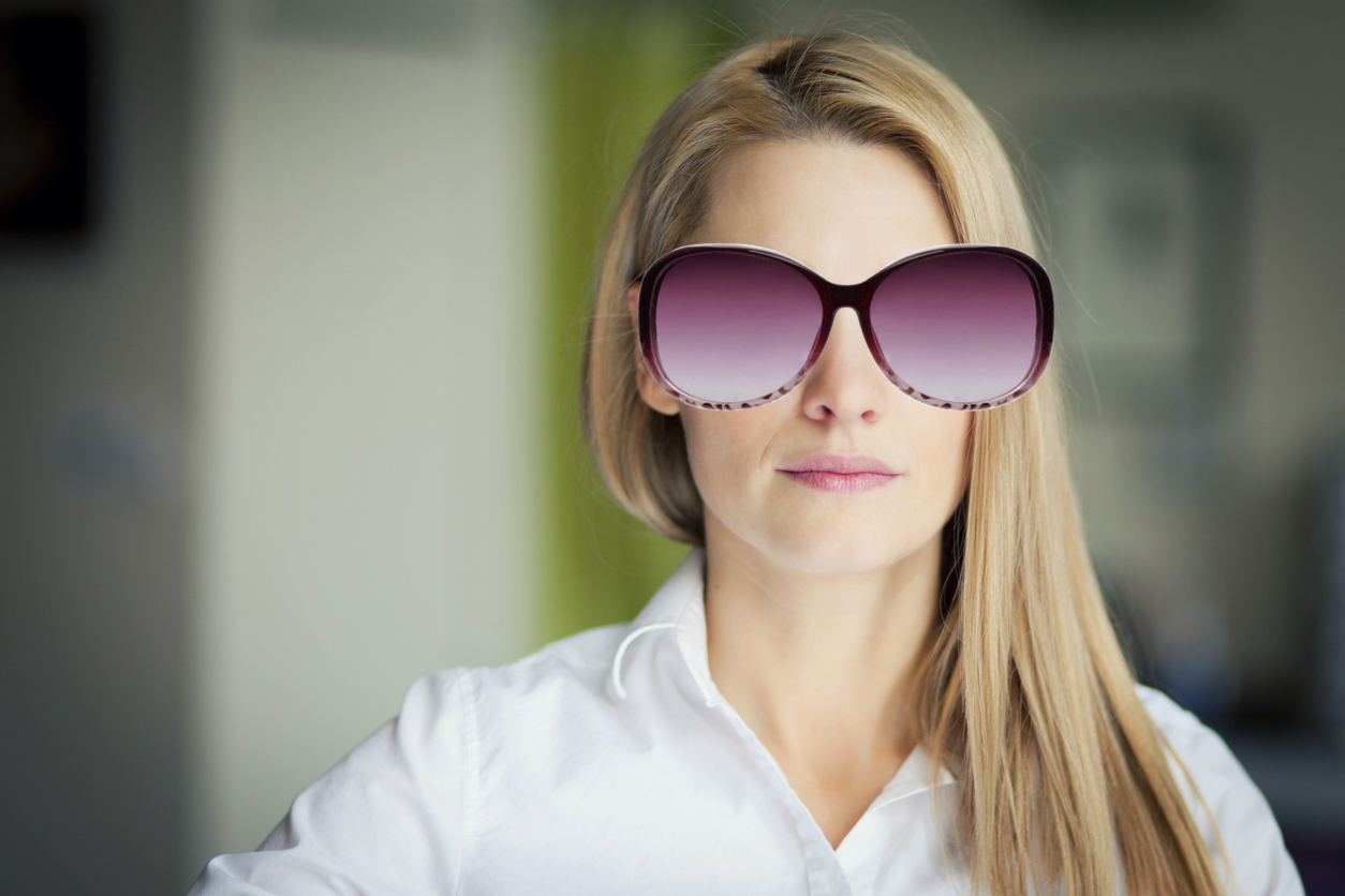 A woman wearing an oversized pair of purple sunglasses