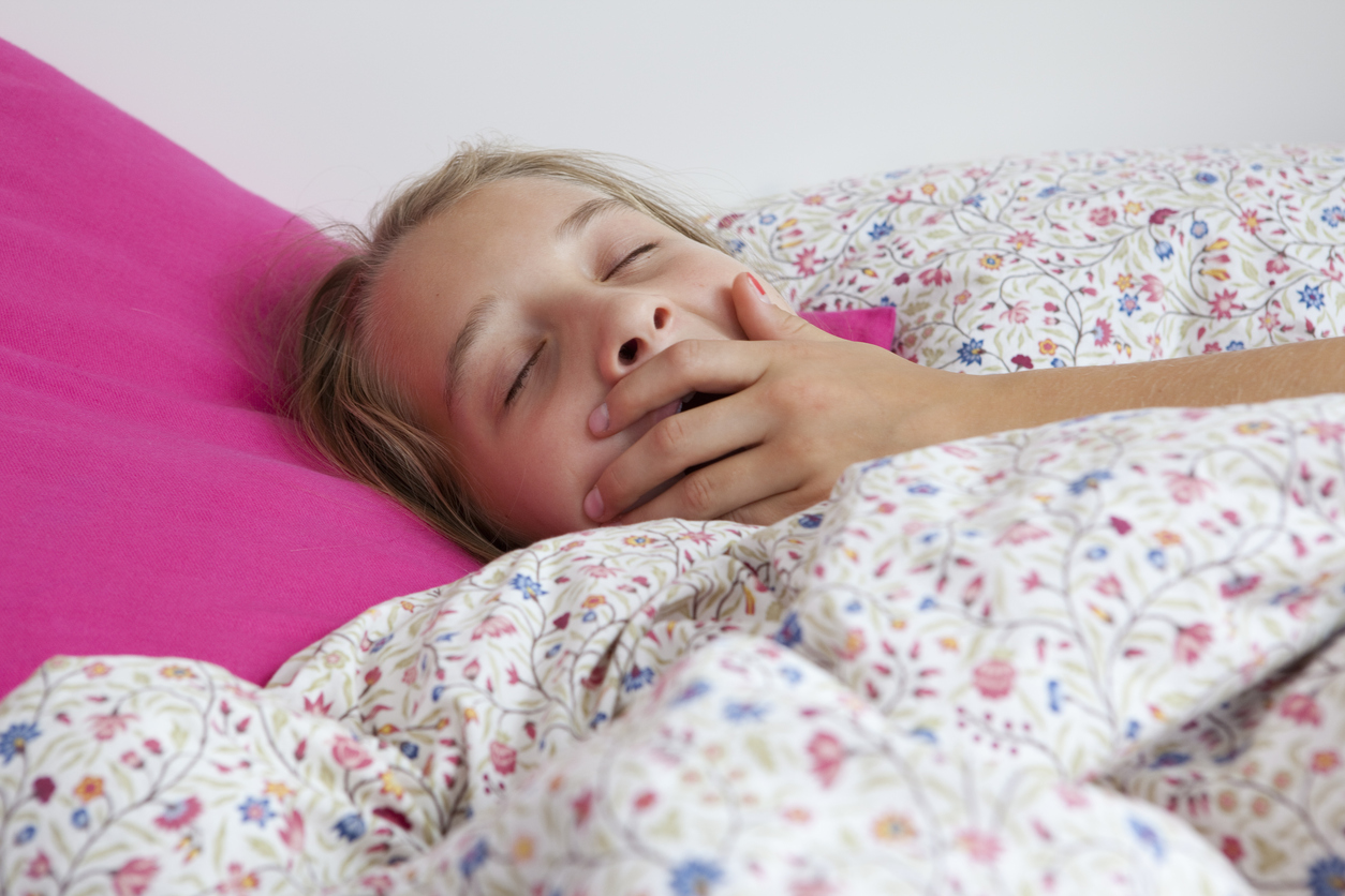 A close up of a child yawning in bed