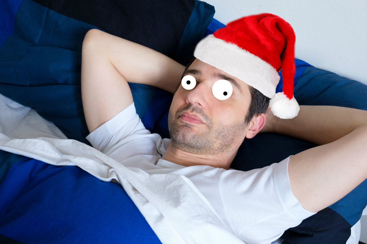 A man in a Santa hat lying in bed thinking about Christmas 