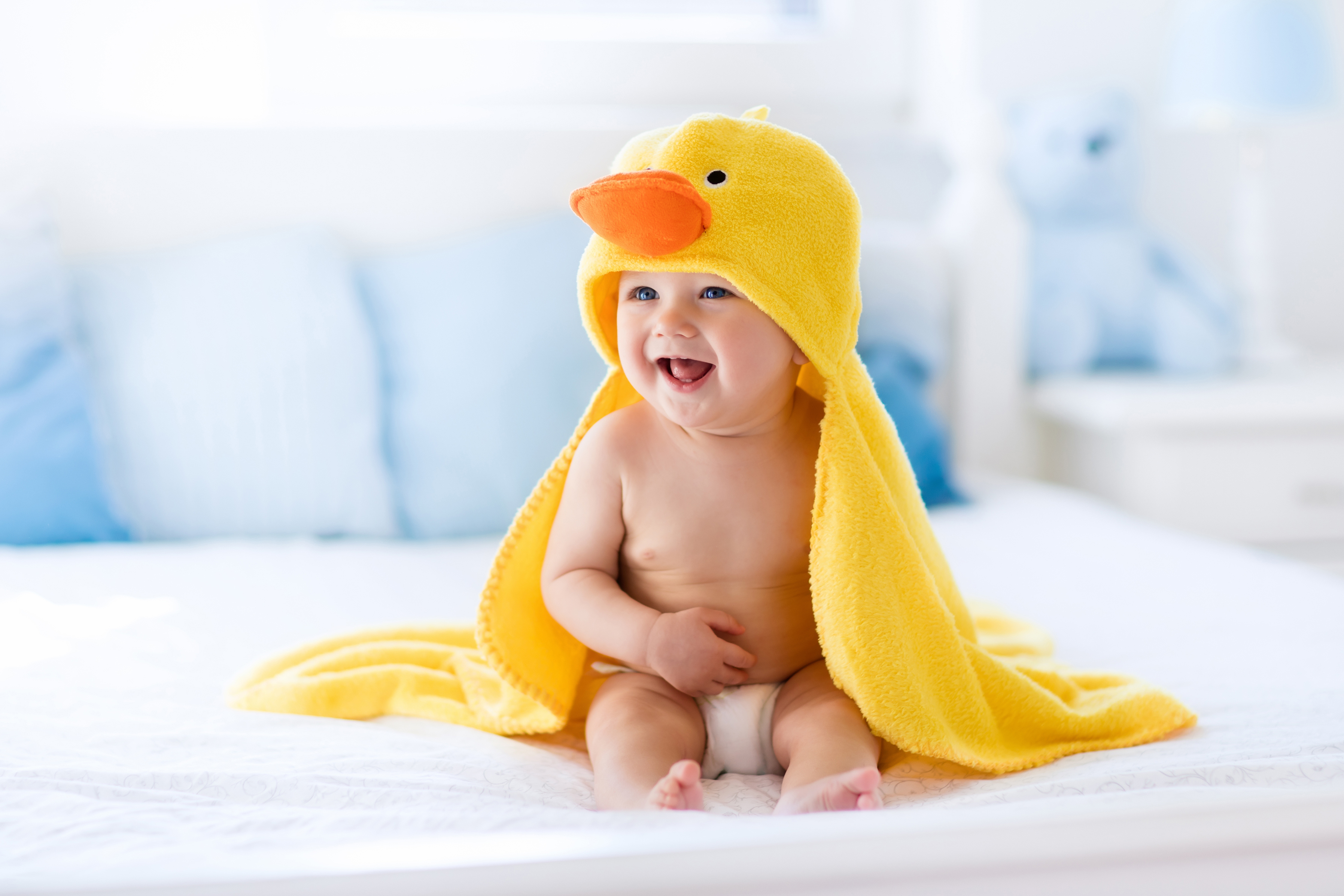 Smiling baby sitting on bed wearing duck costume