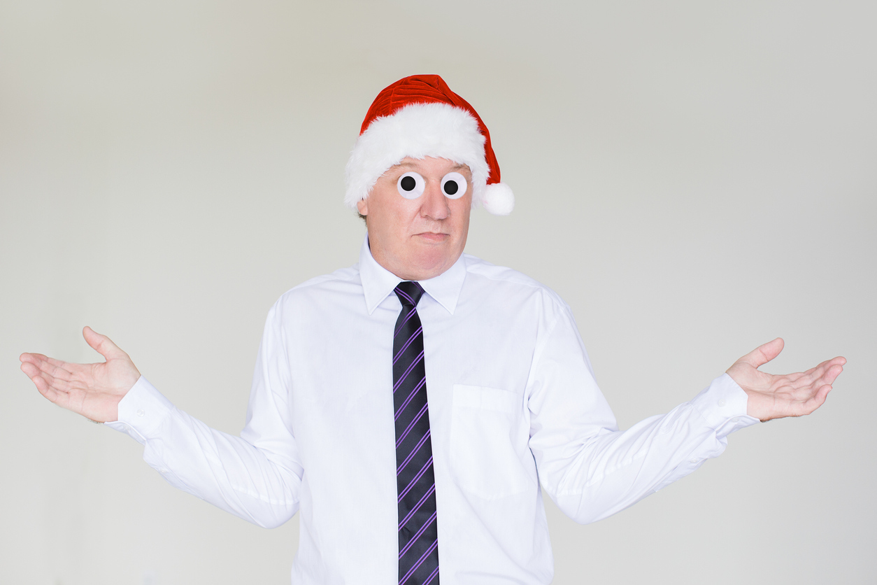 A shrugging man wearing a Santa hat and tie