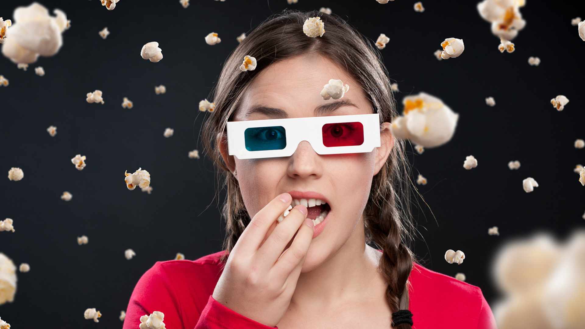A person eating popcorn while wearing old-fashioned 3D glasses 