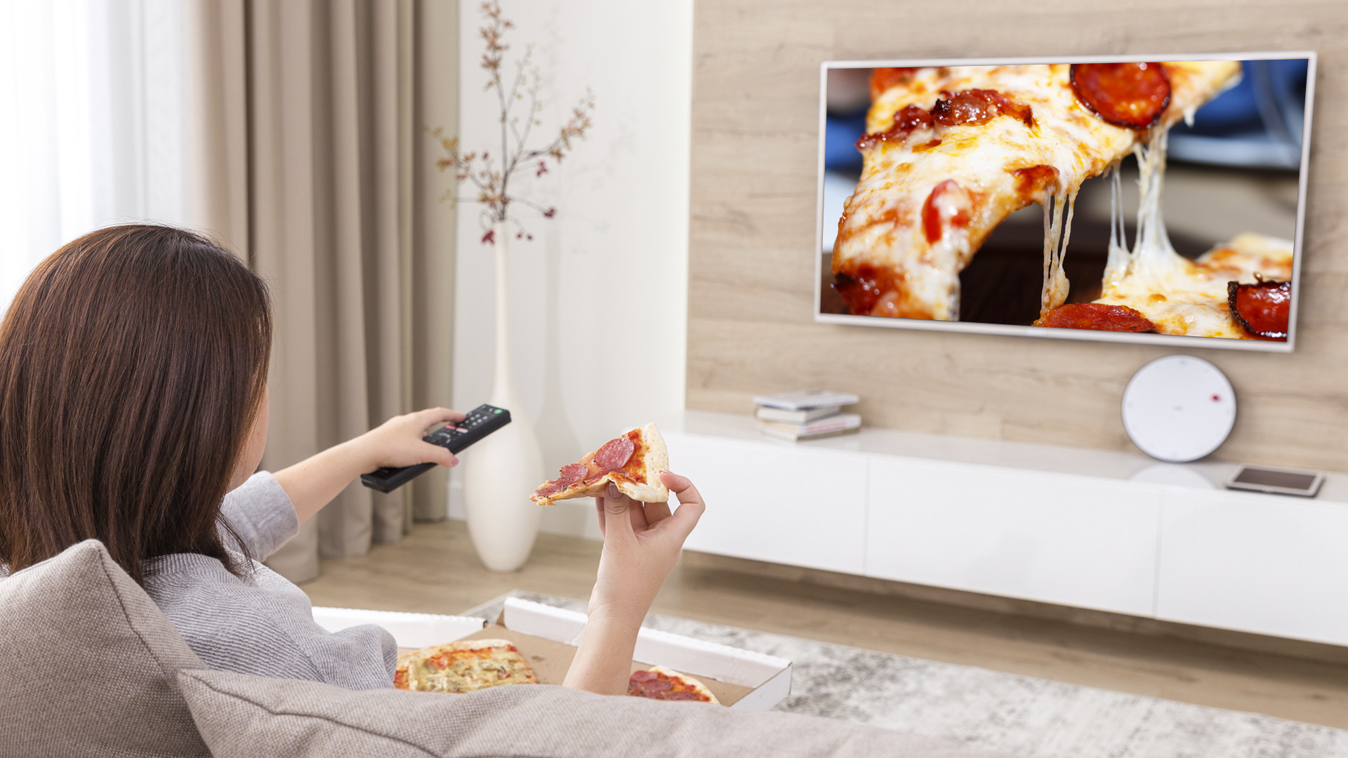 A woman eating a pizza while watching a TV show about pizza
