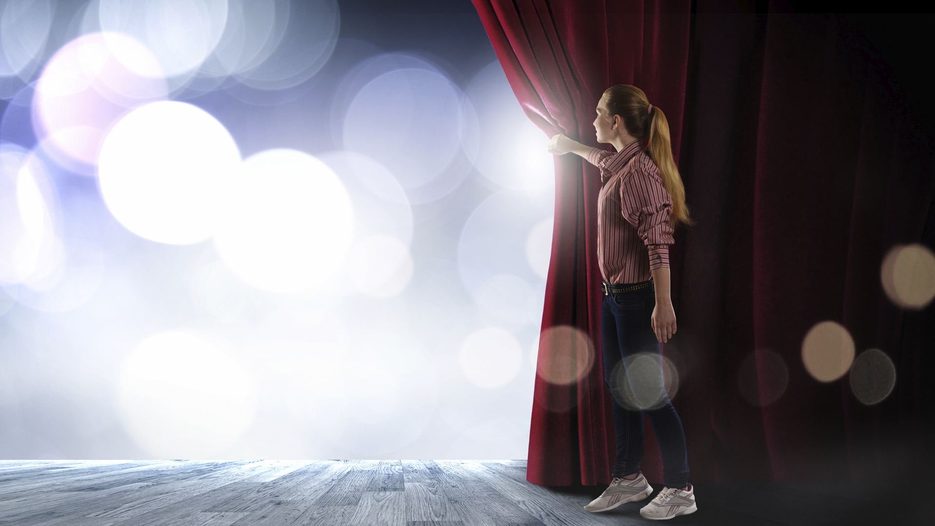 An actor on stage behind a red velvet curtain
