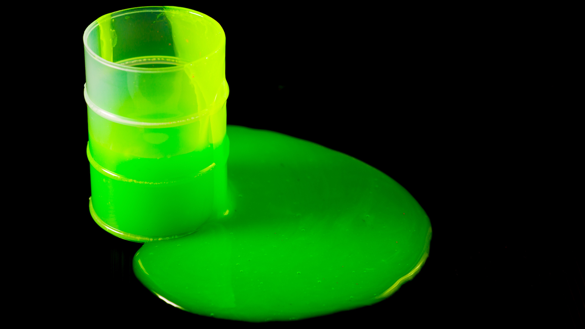 A plastic barrel with green slime oozing out onto the floor