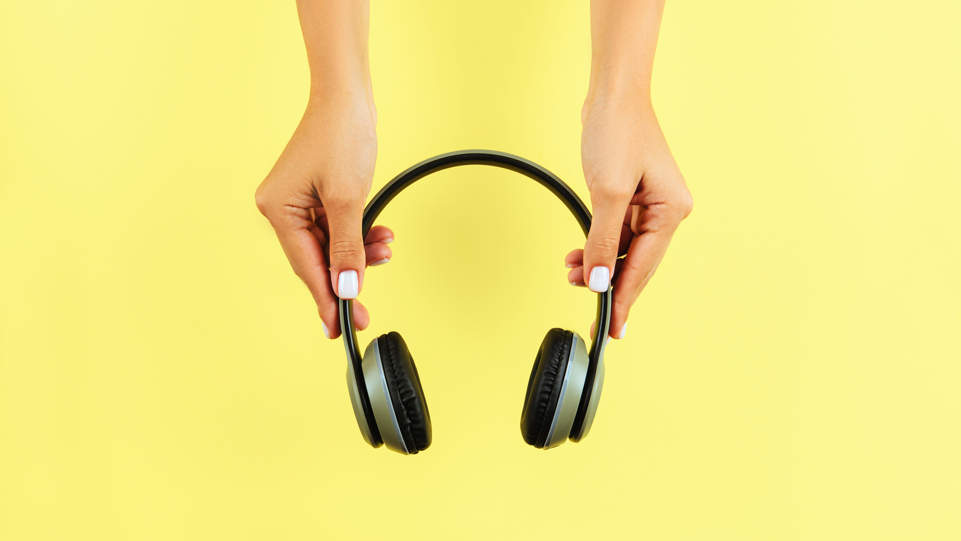 A pair of hands hold some wireless headphones