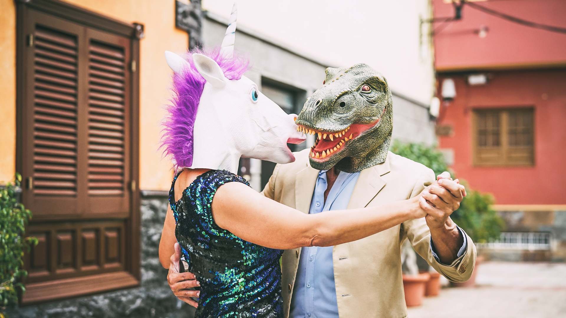 A couple dancing and wearing dinosaur t-rex and unicorn masks