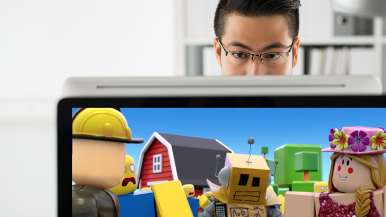 A man on a computer, with a Roblox game in the foreground 