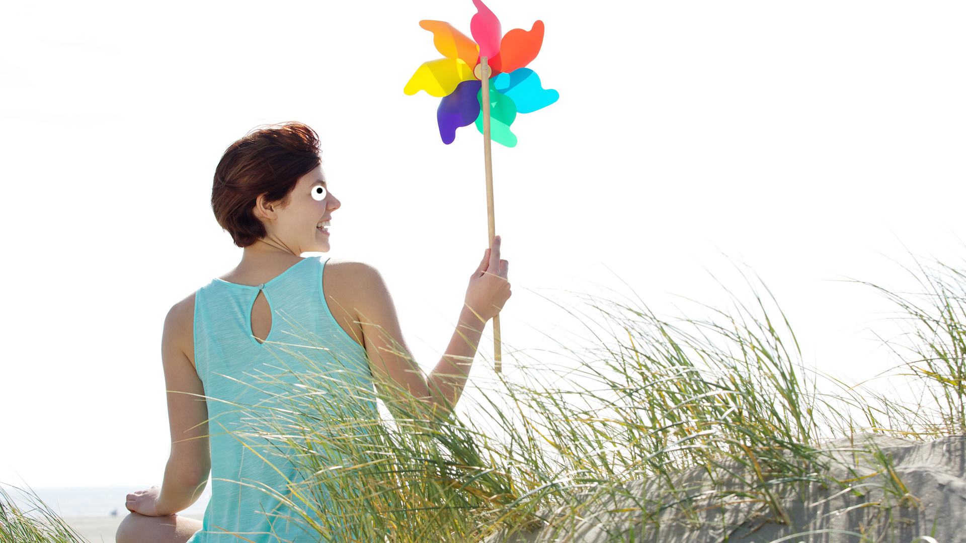 A woman sitting on a sand dune with a colourful pinwheel toy