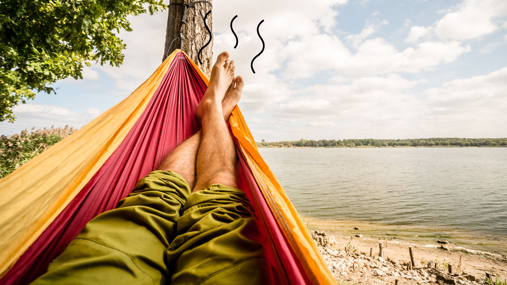A man with stinky feet relaxing in a hammock by a lake