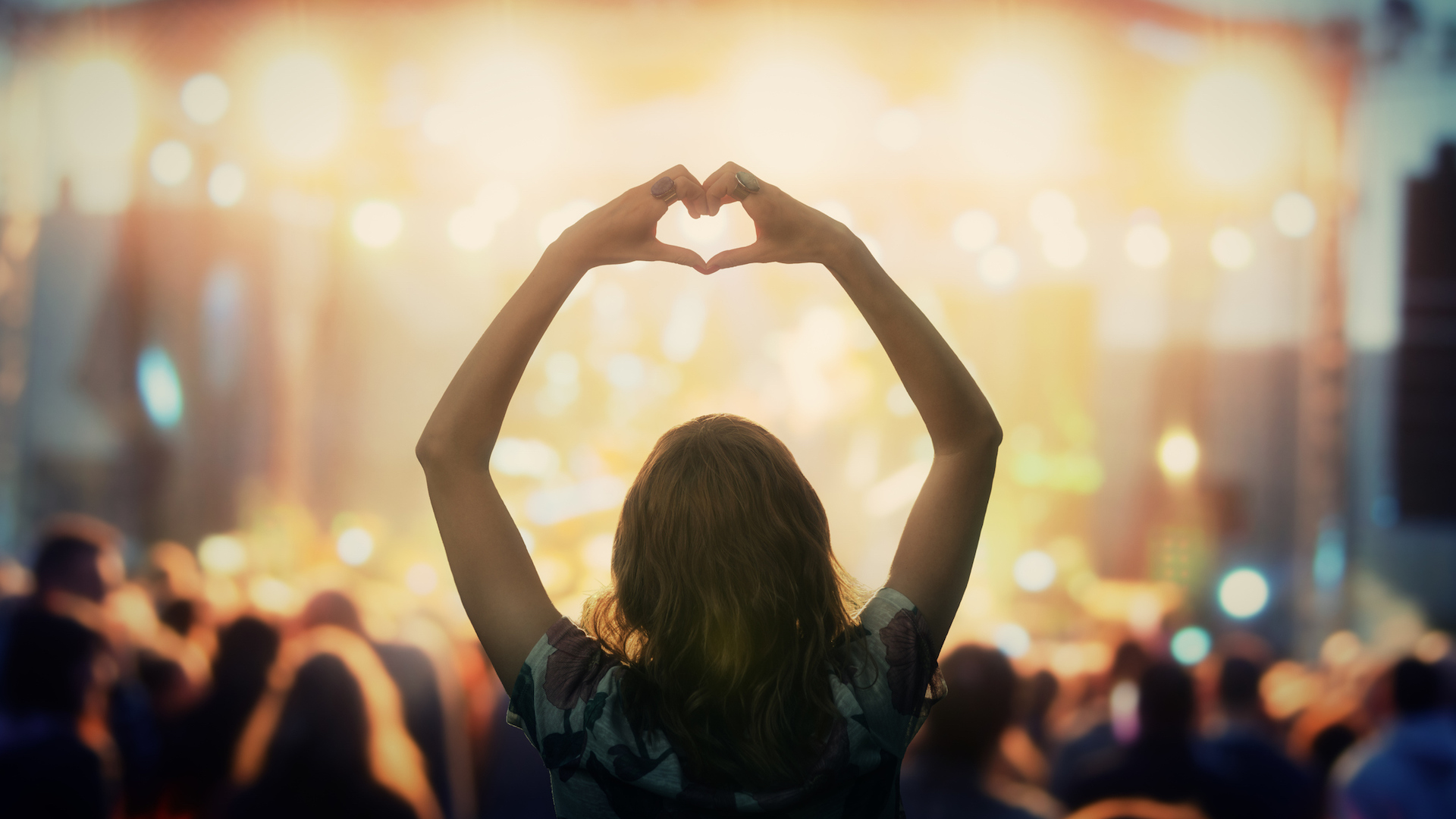 A person making a heart sign at an outdoor concert