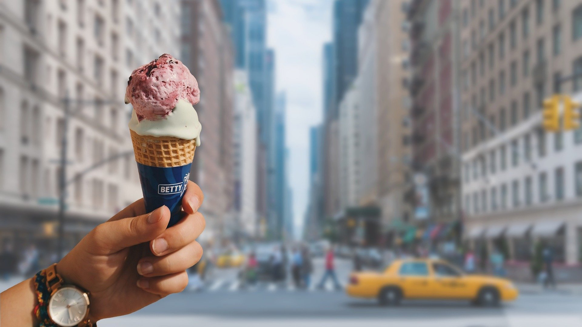 A hand holding an ice cream in a busy New York City street