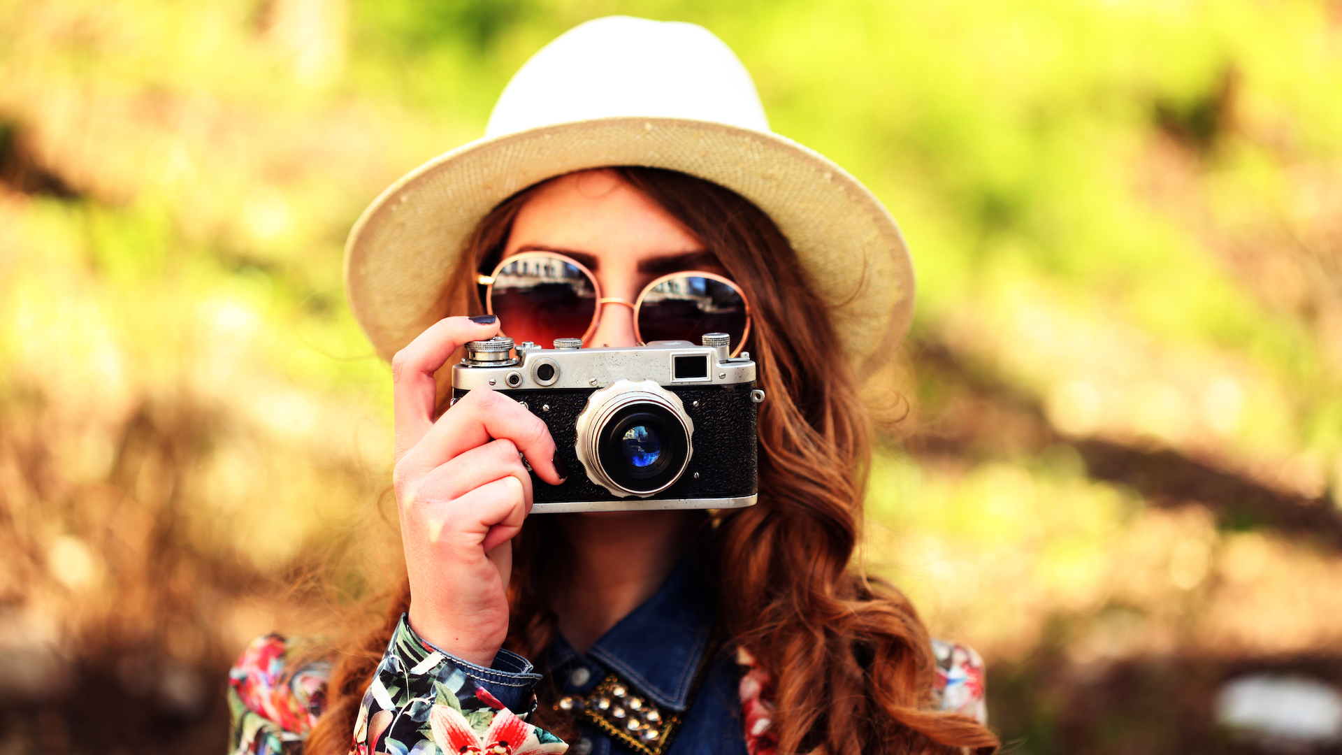 A girl in a hat and sunglasses taking a photograph