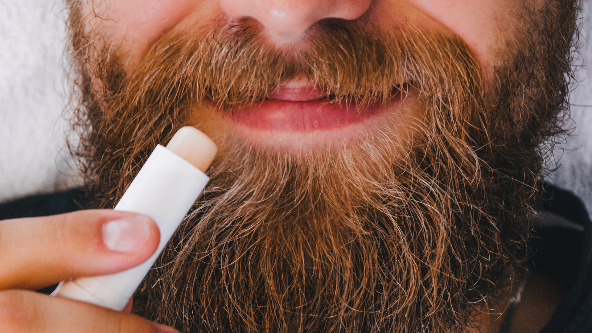 A bearded man putting on some lip balm