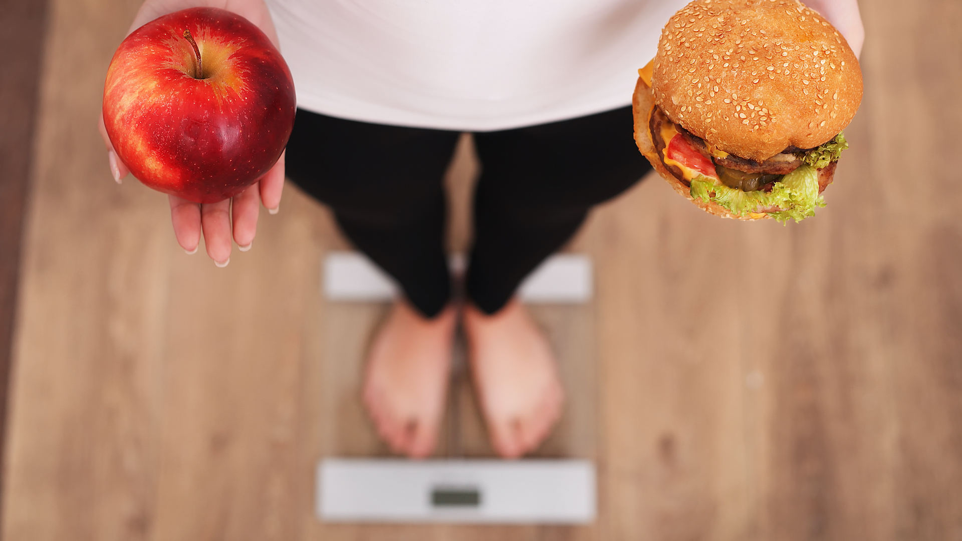 A person holding an apple and a burger on some scales