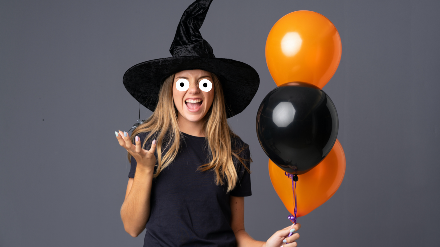 A cackling witch holding some orange and black balloons 
