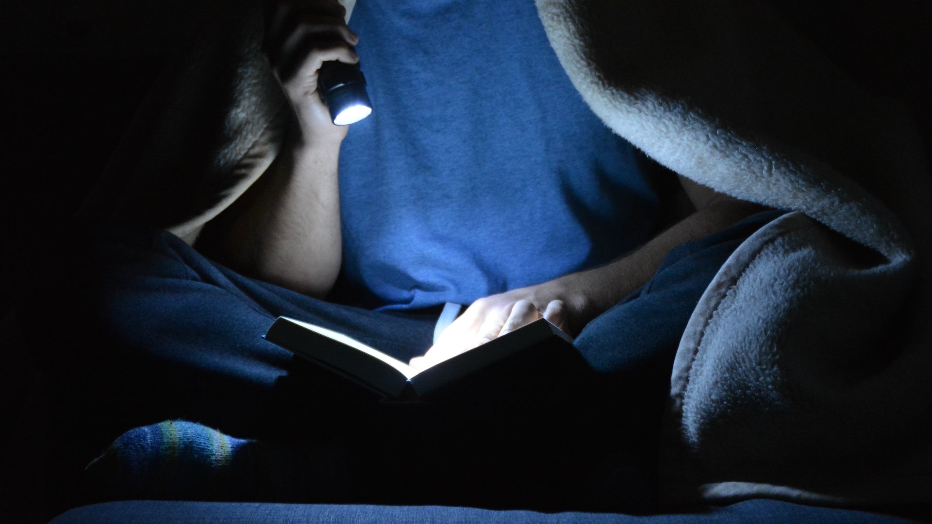 A person using a torch to read a book