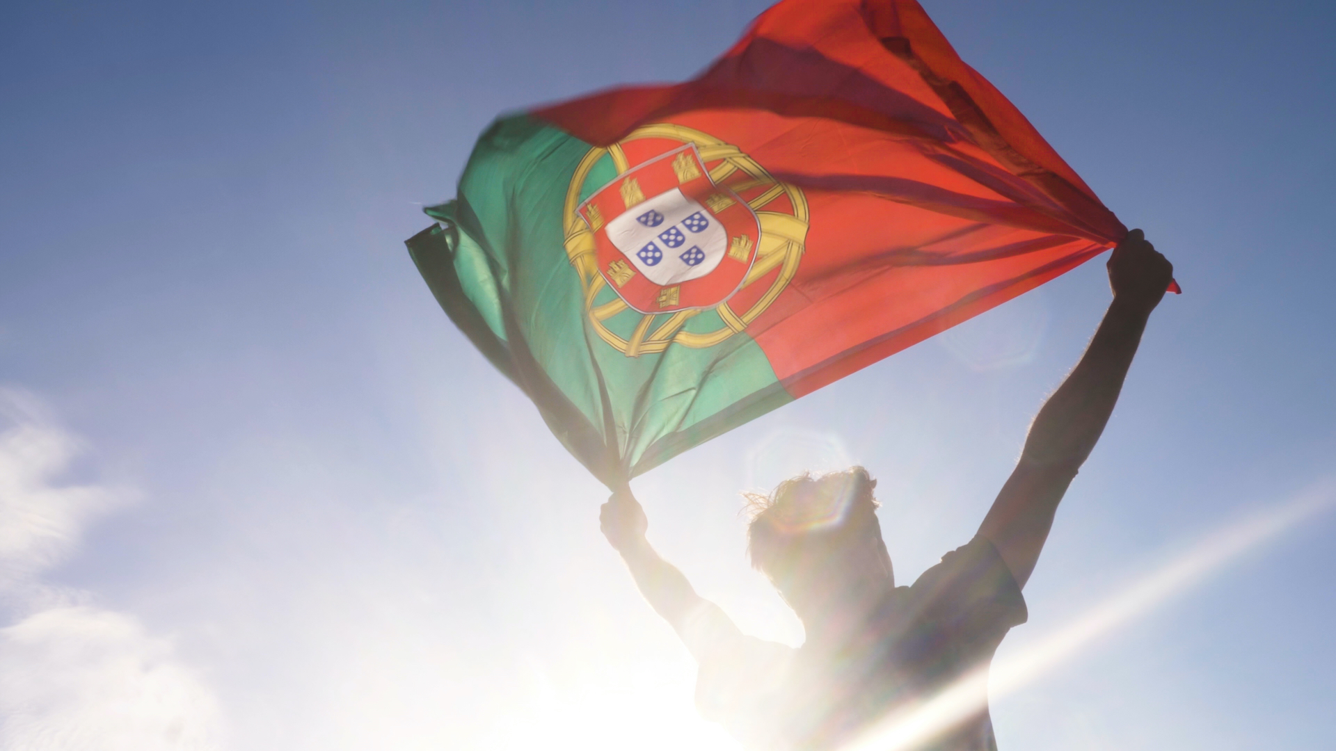 A person holding the Portuguese flag aloft in the sunshine 