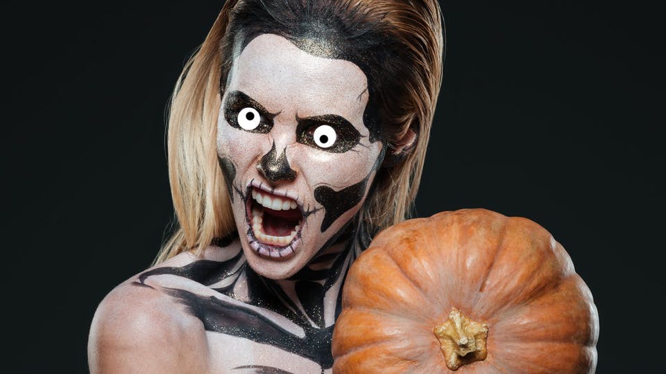 Girl with scary skeleton makeup and pumpkin